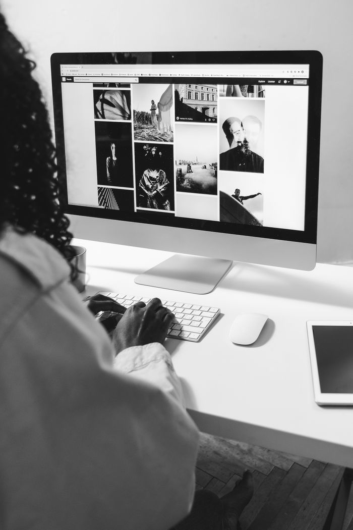 Image en noir et blanc d'une femme afro-américaine anonyme travaillant sur ordinateur à une table avec une tablette